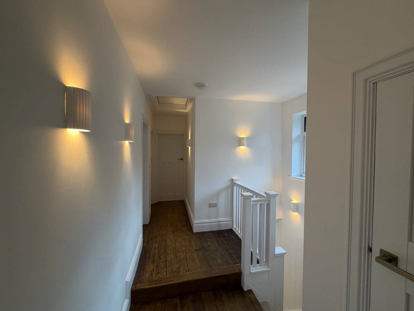 Hallway with wall lighting and oak flooring in a completed new build