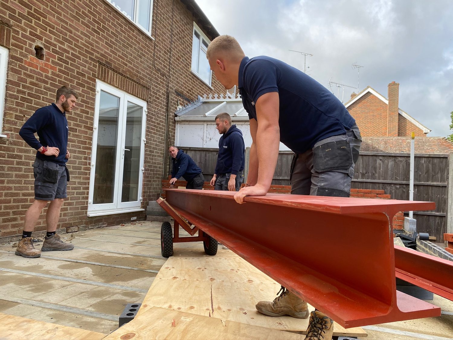 Team moving a painted steel beam into position at the rear of a house