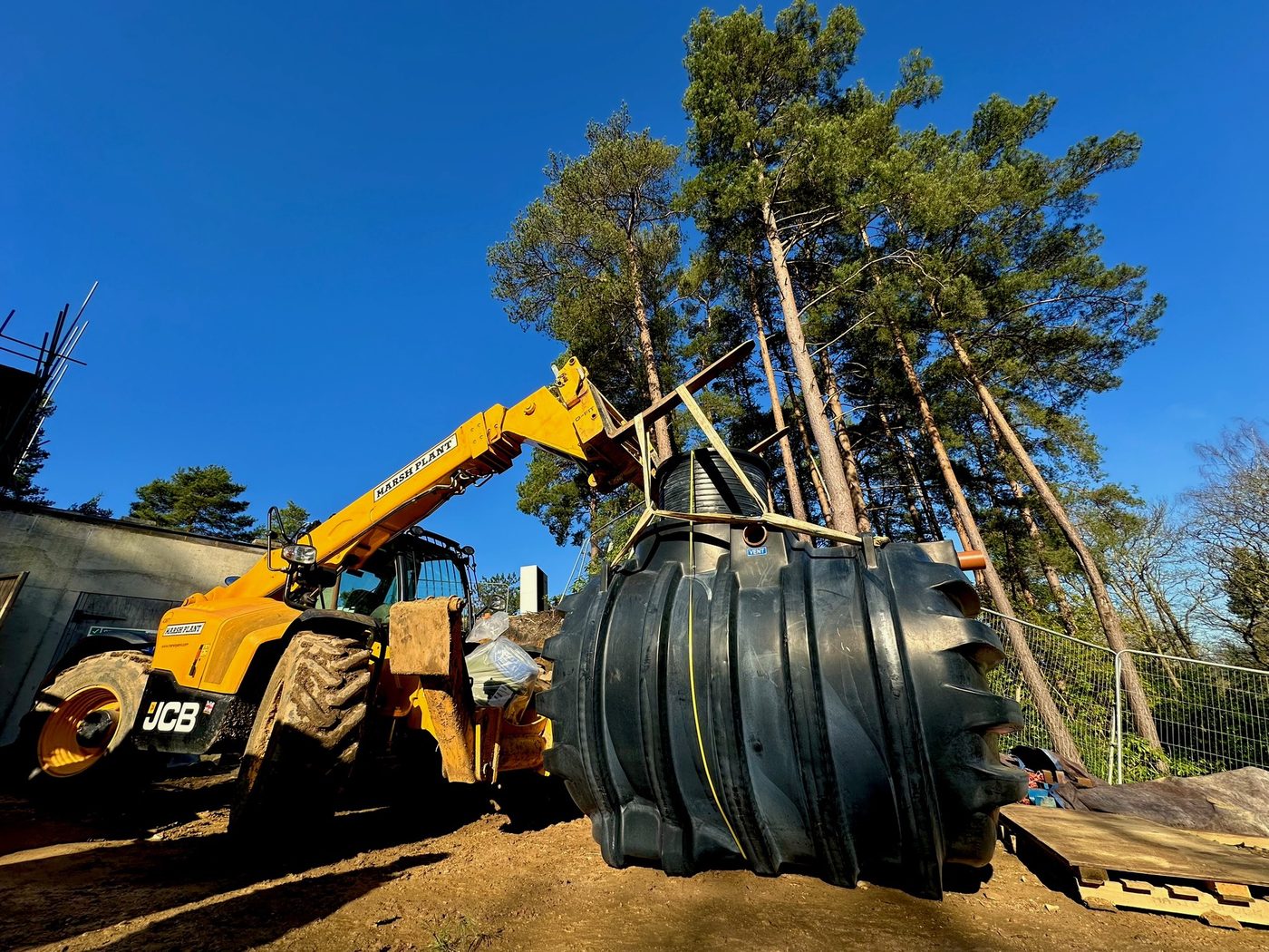 Telehandler lifting a treatment tank into position during groundworks